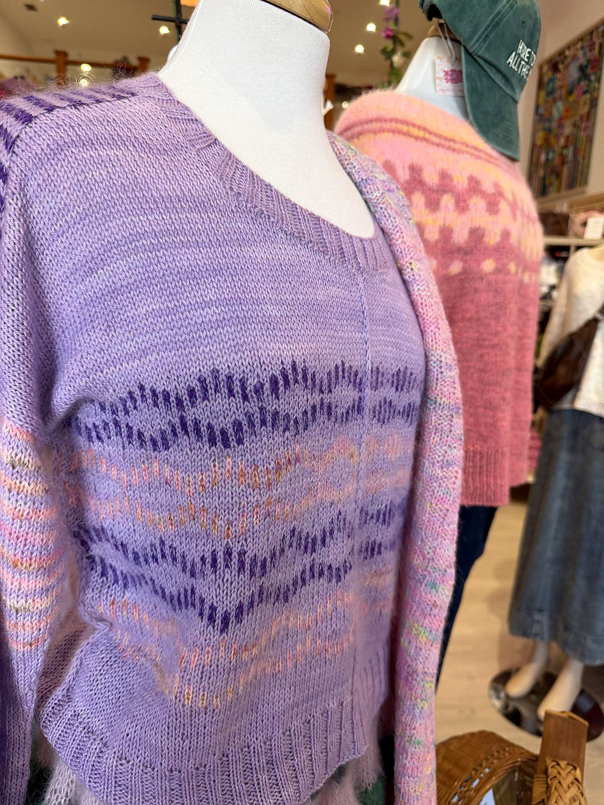 Lavender colorwork sweater on a mannequin at Peaceful Making, with a pink yoke sweater behind it