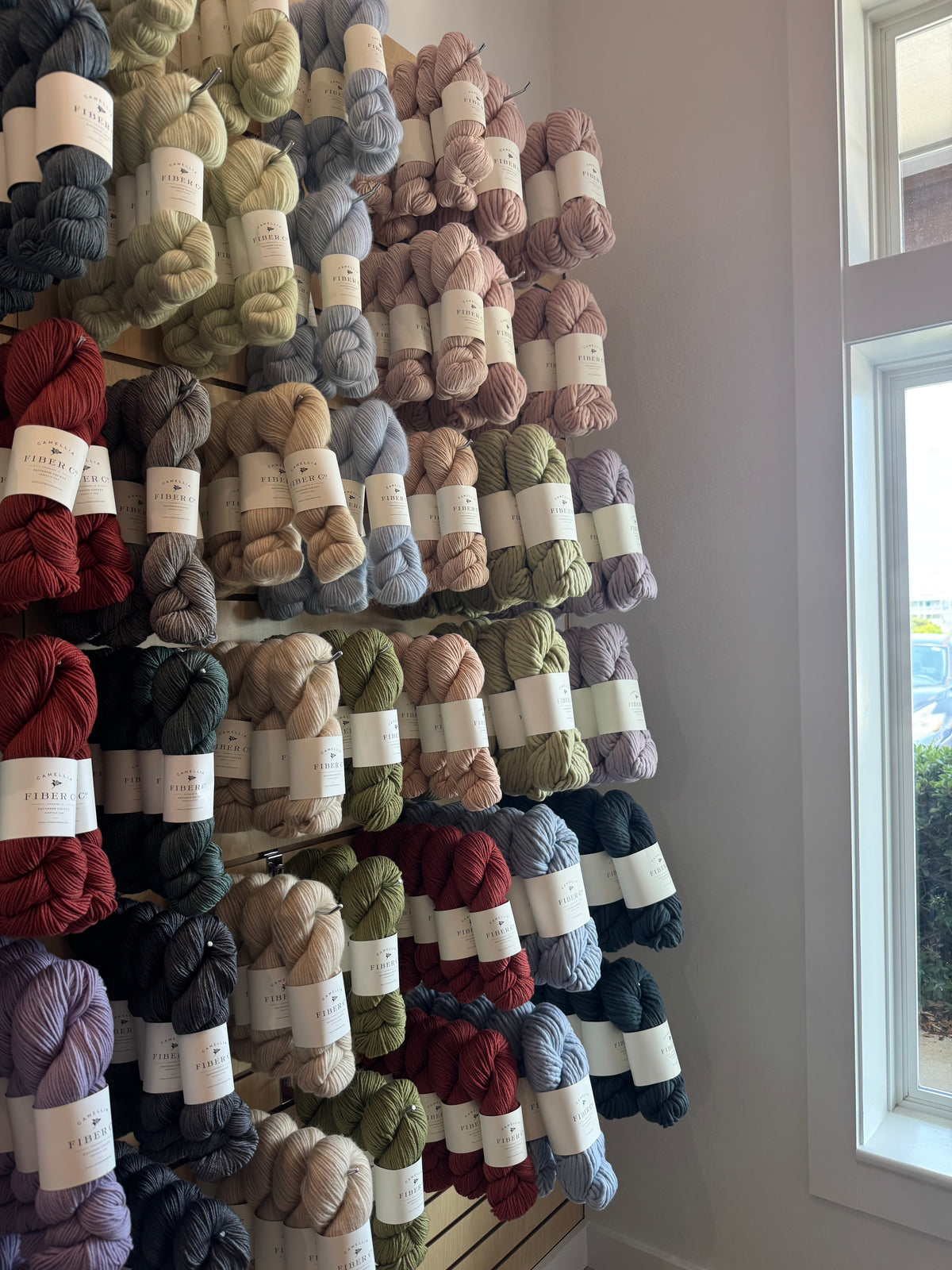 A wall of hand-labeled yarn skeins in reds, greens, blues and naturals at Peaceful Making